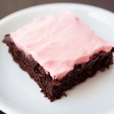 Sliced fudgy brownies with pink frosting and a powdered sugar sprinkle, displayed on a white plate.