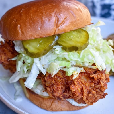 Close-up shot of juicy pickle brined fried chicken sandwich topped with dill pickles and tangy sauce