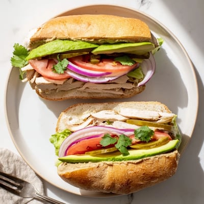 Mexican-style chicken torta sandwich featuring juicy spiced chicken, fresh lettuce, tomato, and pickled jalapeños on soft bread